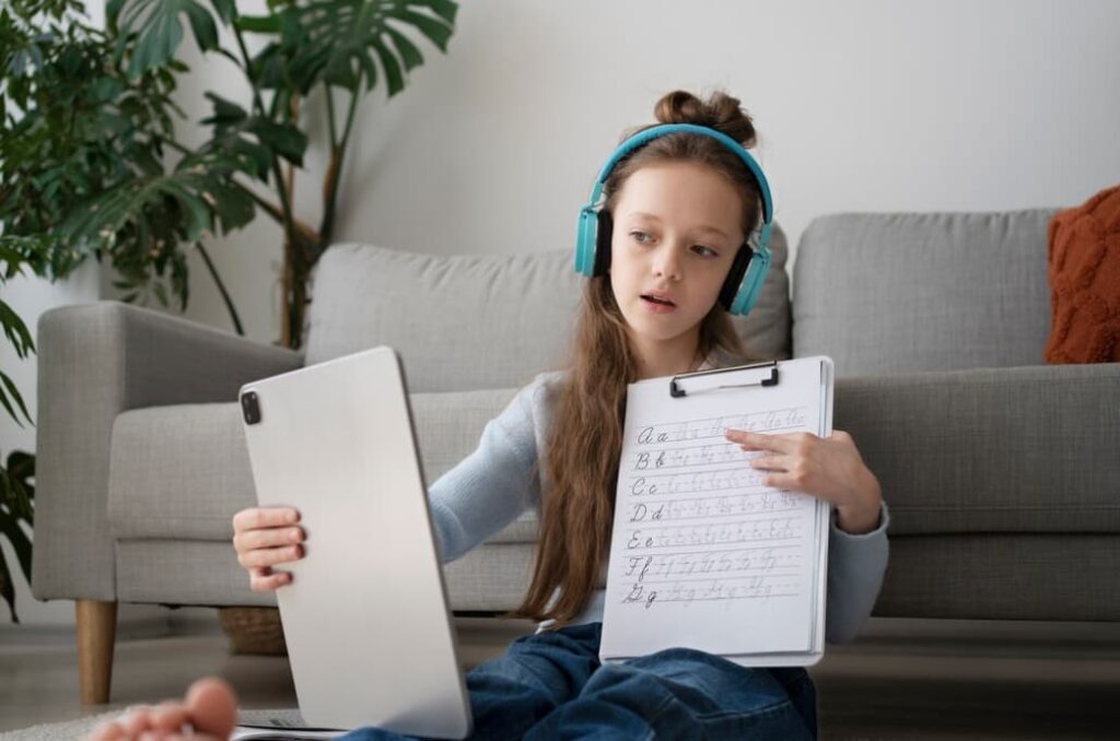 Bambina con cuffie blu mostra un tablet e un foglio con l'alfabeto