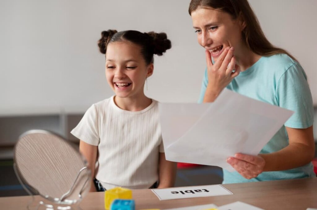 A smiling girl with her speech therapist practicing with flashcards and a mirror