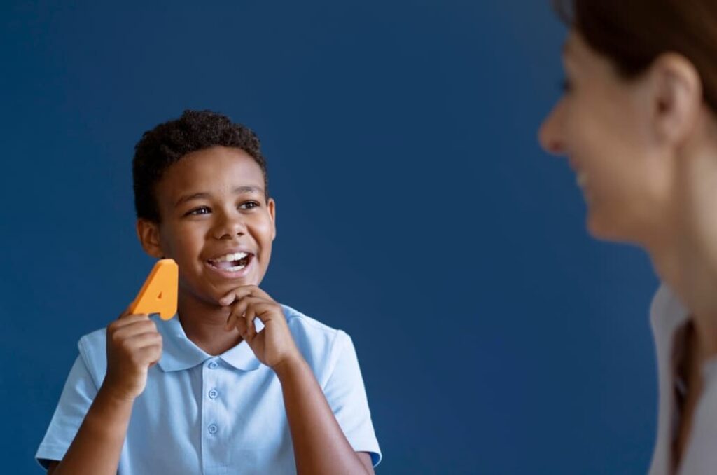 A cheerful young boy holding up a letter 'A' as he learns with a teacher