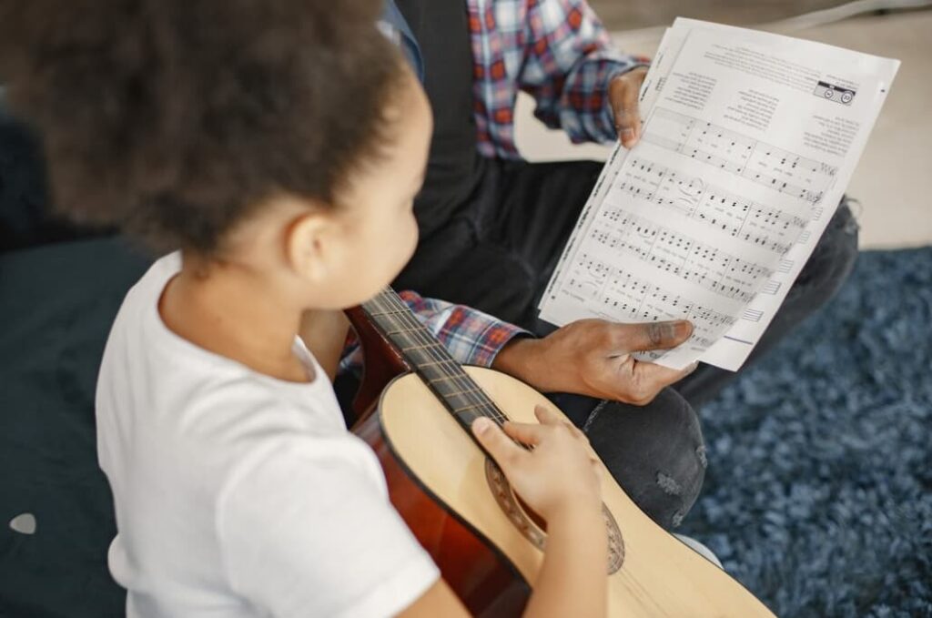 Bambino che impara a suonare la chitarra leggendo uno spartito con un adulto